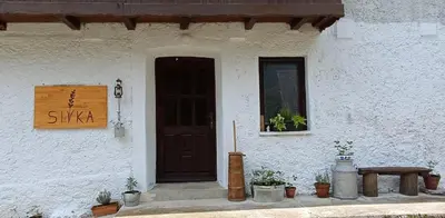 a white building with a black door and a bench at Sivka - mountain apartment with sauna in Kobarid