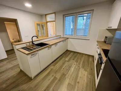 a kitchen with white cabinets and wooden floors and windows at Apartment Neli in Rečica ob Savinji