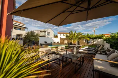 a patio with an umbrella and chairs and a pool at Villa Sunset Pool & Spa apartments in Zgornje Škofije