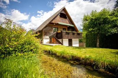 a house on a hill with a stream in front of it at Apartma Metka in Bohinj