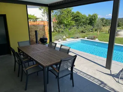 a table and chairs on a patio with a swimming pool at Holiday house Oljka in Kobdilj
