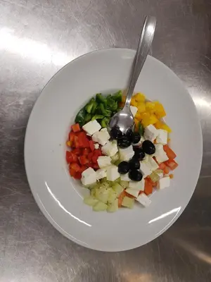a white plate with a bowl of vegetables with a spoon at Guesthouse Pri Štefanu in Most na Soči
