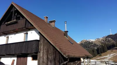 a wooden barn with a brown roof on a mountain at Apartments Relax Jezerca in Cerklje na Gorenjskem