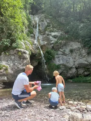 a man and two children playing in a stream with a waterfall at Hiša za Gradom in Kobarid