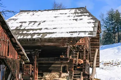 an old wooden barn with snow on the roof at Quiet apartment with a terrace on Organic farm in Prevalje