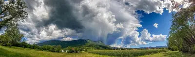 a cloudy sky with a green field and a mountain at Apartment Otava in Šempas