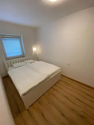 a white bedroom with a bed and a window at Ada Apartment in Ljubljana