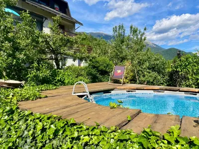 a pool with a wooden deck next to a house at Apartma Zeus in Jesenice