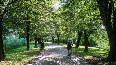two people riding bikes down a path in a park at Valetier apartments in Ljubljana