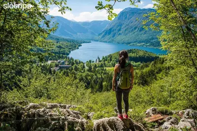 a woman with a backpack standing on a hill overlooking a lake at APARTMA VODNIK in Bohinj