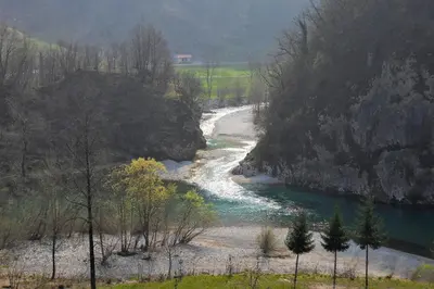 a river with a rocky shoreline next to a mountain at Apartment Sotočje in Dolenja Trebuša