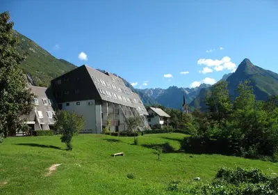 a building in a field with mountains in the background at BovecEnter Apartments Kaninska vas in Bovec