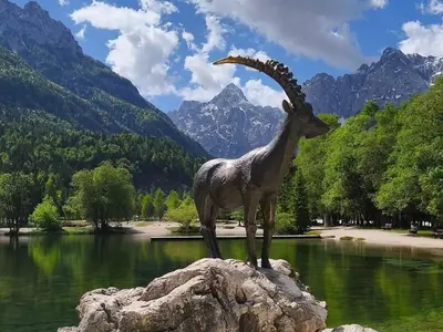 a statue of a goat standing on a rock near a lake at Riverside Apartma 1, Kranjska Gora in Kranjska Gora
