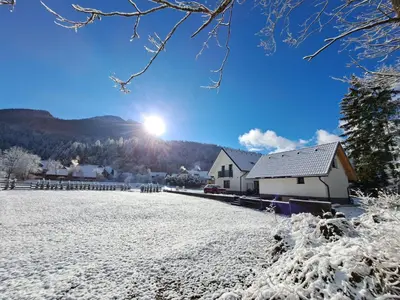a house in the snow with the sun in the background at Riverside Apartma 2, Kranjska Gora in Kranjska Gora