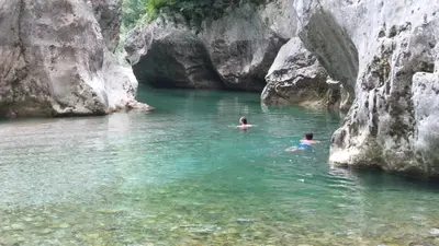 two people swimming in a river next to some rocks at Apartma Kresnička in Kobarid