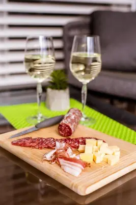 a wooden cutting board with cheese and two glasses of wine at Apartma Sofija, Moravski Dvori in Moravske Toplice