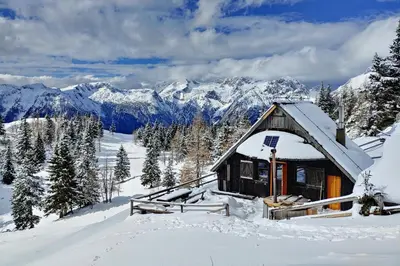 a small cabin in the snow with mountains in the background at Chalet Zlatica Velika Planina in Stahovica