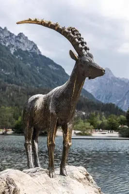 a statue of a goat standing on a rock near water at EROS APARTMENT Kranjska Gora in Kranjska Gora