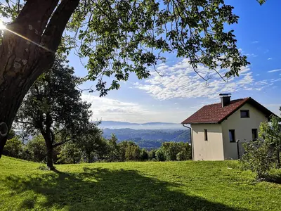 a white house on a hill with a green field at Apartma Hiša na Ravnah with hot tub in Pišece
