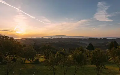 a sunset over a field with trees and mountains at Apartma Hiša na Ravnah with hot tub in Pišece
