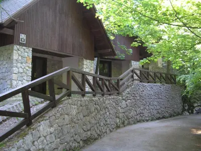 a building with a stone wall and a wooden staircase at Camping Pivka Jama Postojna in Postojna