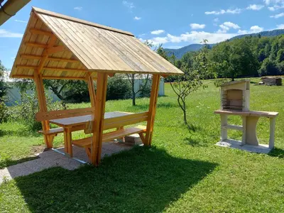 a wooden gazebo with a grill in a field at Apartma Markelj in Radovljica