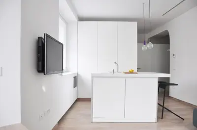 a kitchen with white cabinets and a tv on a wall at Studio Emmi in Ljubljana