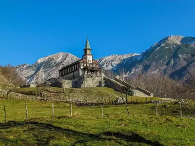 an old building on a hill with mountains in the background at Vilijev Raj, a property with cottage in the countryside in Avče
