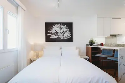 a bedroom with a white bed and a kitchen at Romantic JUMP Studio overlooking river, free parking in Ljubljana