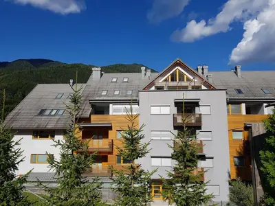 a large white building with trees in front of it at Apartment Lesnina in Kranjska Gora