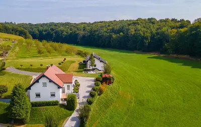 a white house in a green field with a driveway at POD OREHI - Hiša na podeželju - RAZPRŠENI HOTEL Jeruzalem Slovenija in Miklavž pri Ormožu