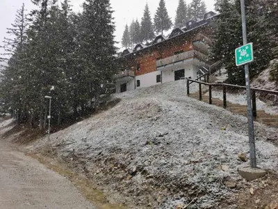 a snow covered hill next to a building with a street sign at Apartma Med smrekami Golte in Mozirje