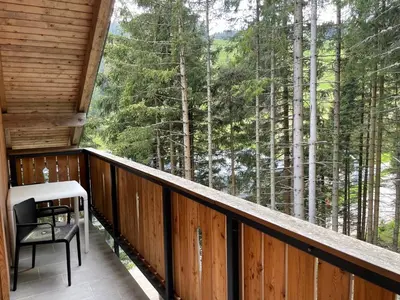 a balcony with a table and a chair and trees at Apartma Med smrekami Golte in Mozirje