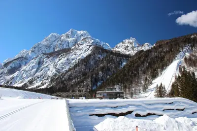 a snow covered mountain with a house in the foreground at Apartments Koblar in Kranjska Gora