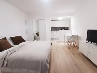 a white bedroom with a bed and a kitchen at Apartments Bassanese in Bled