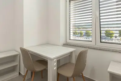 a white table and chairs in a room with two windows at RM Roma Studio in Celje
