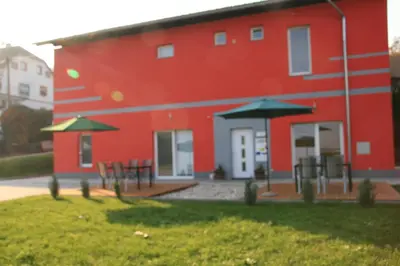 a red building with tables and umbrellas in front of it at Apartments Pri Adamsovih in Čatež ob Savi