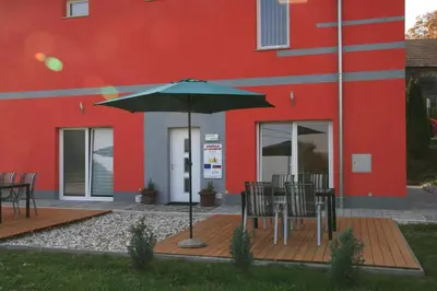 a table with an umbrella in front of a red building at Apartments Pri Adamsovih in Čatež ob Savi