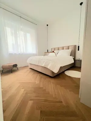 a white bedroom with a large bed and wooden floors at Apartment Tivoli in Ljubljana