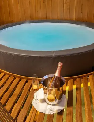 a bottle of wine and two glasses on a table next to a tub at Vineyard Cottage Krivic in Trebelno
