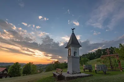 a clock tower in a field with a sunset in the background at Vineyard Cottage Krivic in Trebelno