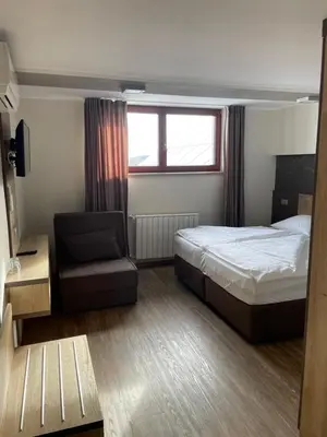 a bedroom with a bed and a chair and a window at Hotel Roškar in Ptuj