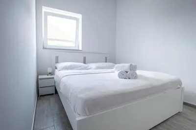 a white bedroom with a large white bed with a window at 2022 Central Apartment Maribor (Garden + Parking) in Maribor