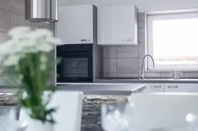 a white kitchen with a sink and a vase of flowers at 2022 Central Apartment Maribor (Garden + Parking) in Maribor