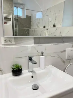 a white bathroom with a sink and a mirror at Under Castle Apartment in Ljubljana