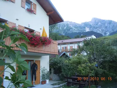 a building with flowers on the balcony with mountains in the background at Apartment Rakušček in Kobarid