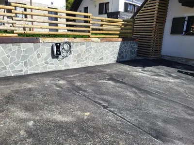 a stone retaining wall next to a house with a fence at Apartments Nune 2 in Zreče