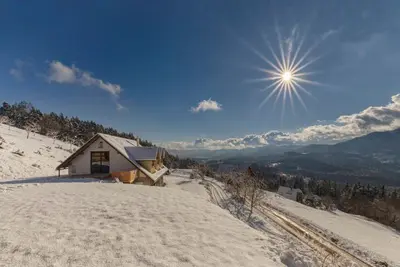 a house on a snowy hill with the sun in the sky at Guest House Štruc in Slovenj Gradec