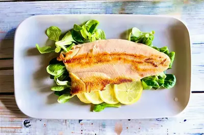 a white plate with a piece of fish and greens at Gostišče Barbara in Idrija