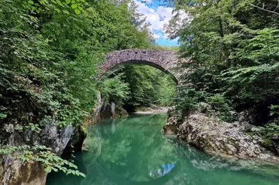 a stone bridge over a river with green water at Mobilna hiška Lebanč in Breginj